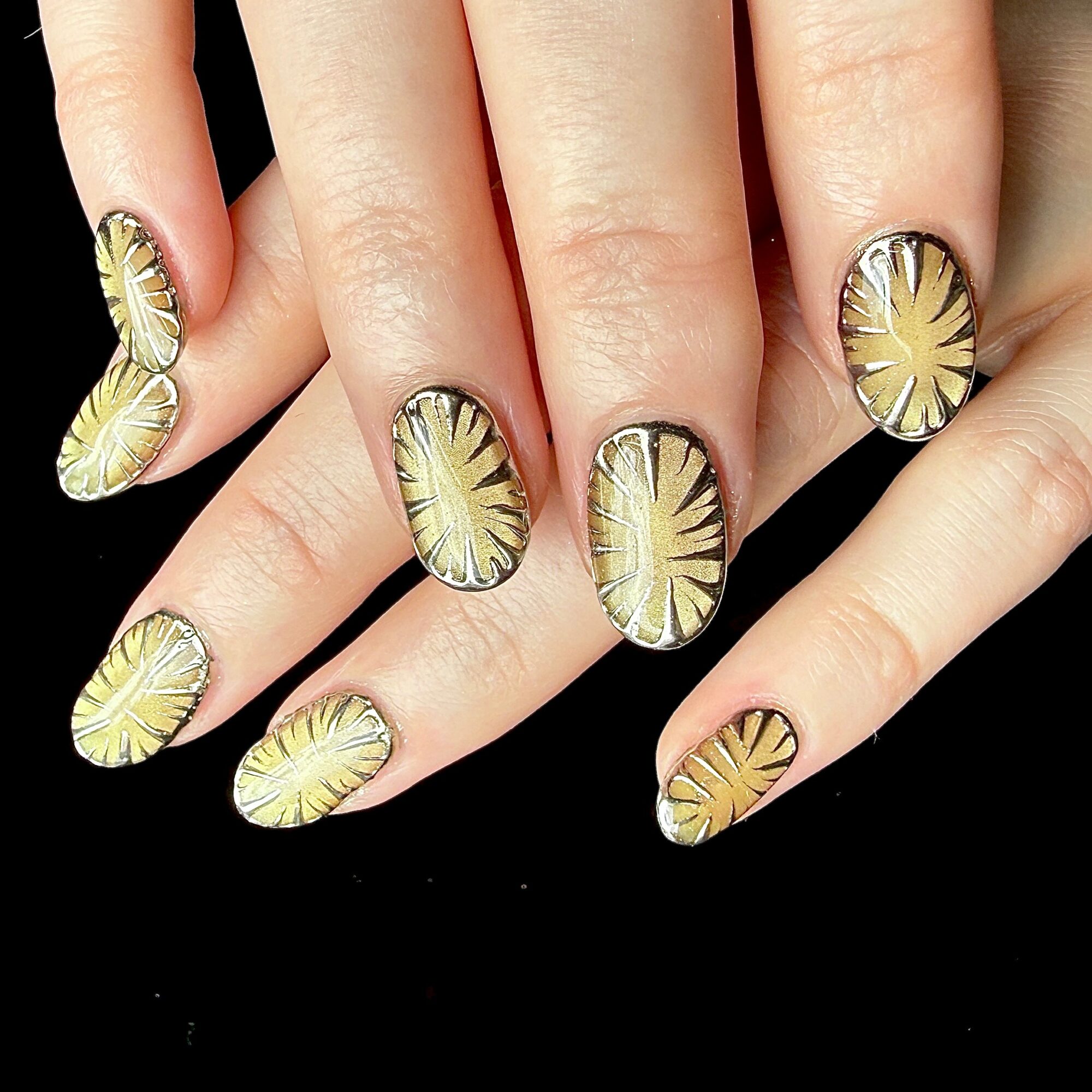 Nail art with yellow and black sunburst design on fingernails, black background, five fingers visible, detailed pattern.