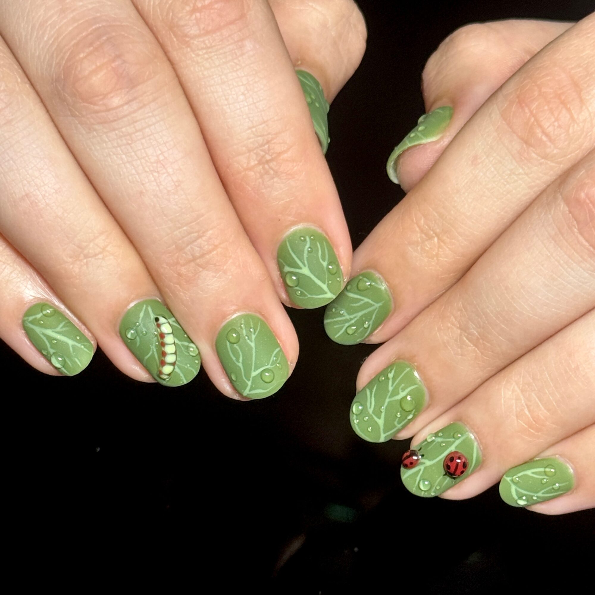 Hands with green nail polish and holiday-themed designs, including ladybugs and decorative patterns, against a black background.
