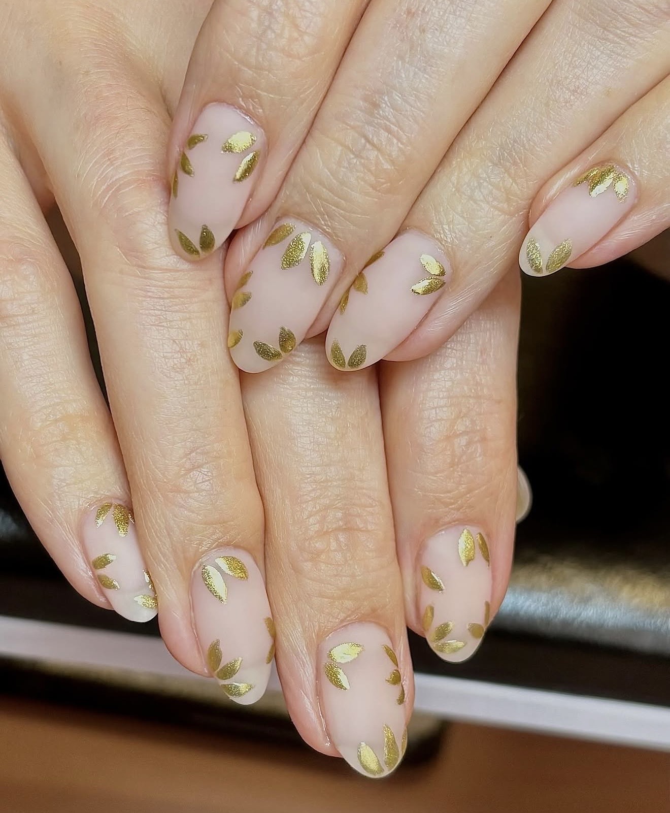 Close-up of hands with nails painted in a light color, decorated with small green leaf patterns.