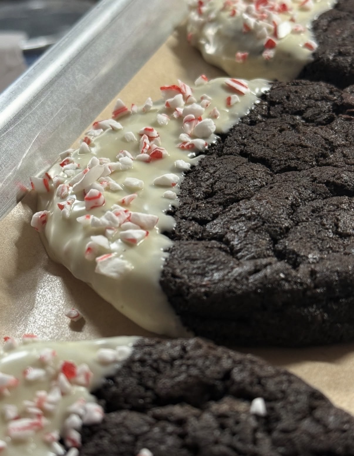 Chocolate cookies with white chocolate and peppermint topping on parchment paper, with a metal tray nearby.