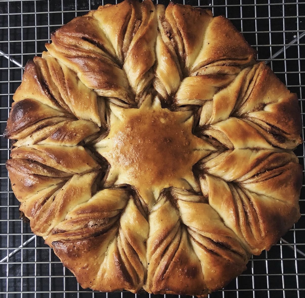 Star-shaped baked bread with twisted sections, golden-brown crust, on a wire cooling rack.
