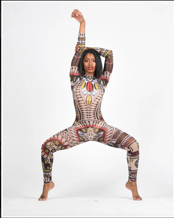 Woman in colorful patterned bodysuit poses with arms raised and legs apart against a white background.