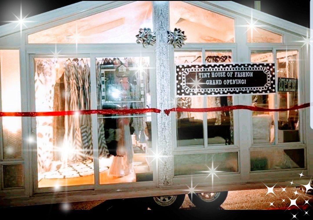 Storefront with large glass windows, sign for grand opening, and interior clothing displays, illuminated at night.