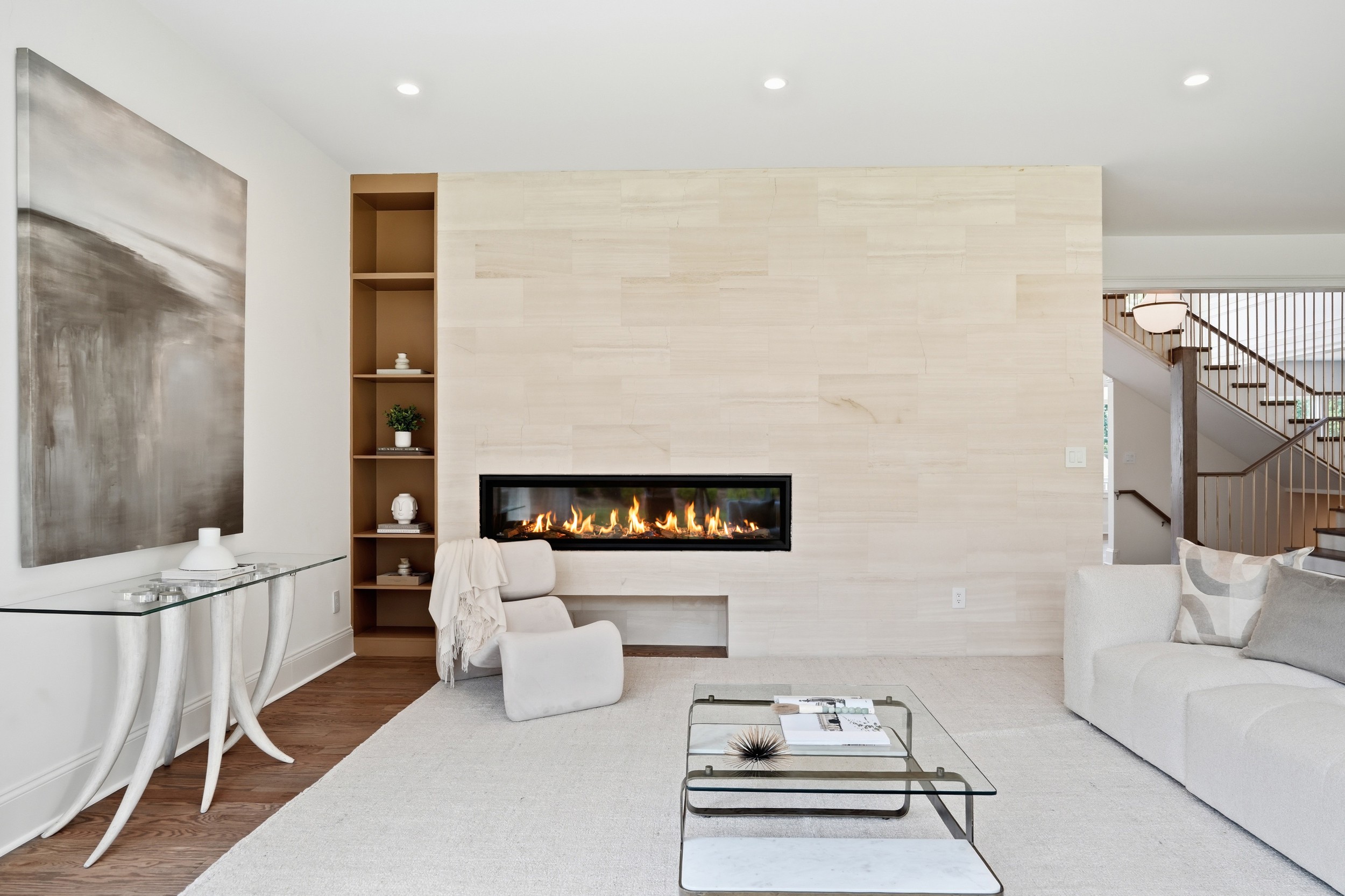Living room with a modern fireplace, white furniture, and a large abstract painting on the wall.