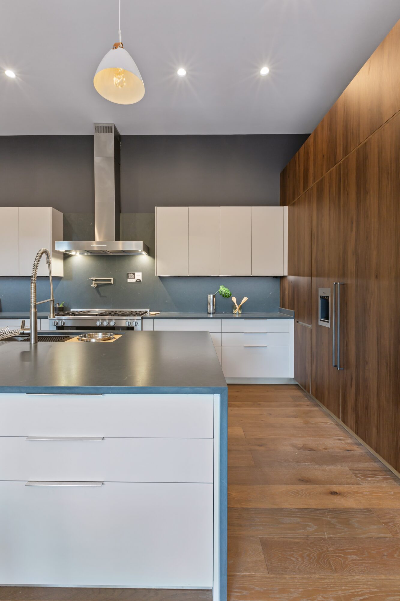 Modern kitchen with white cabinets, a blue backsplash, and wooden wall paneling, featuring a ceiling light and stainless steel appliances.