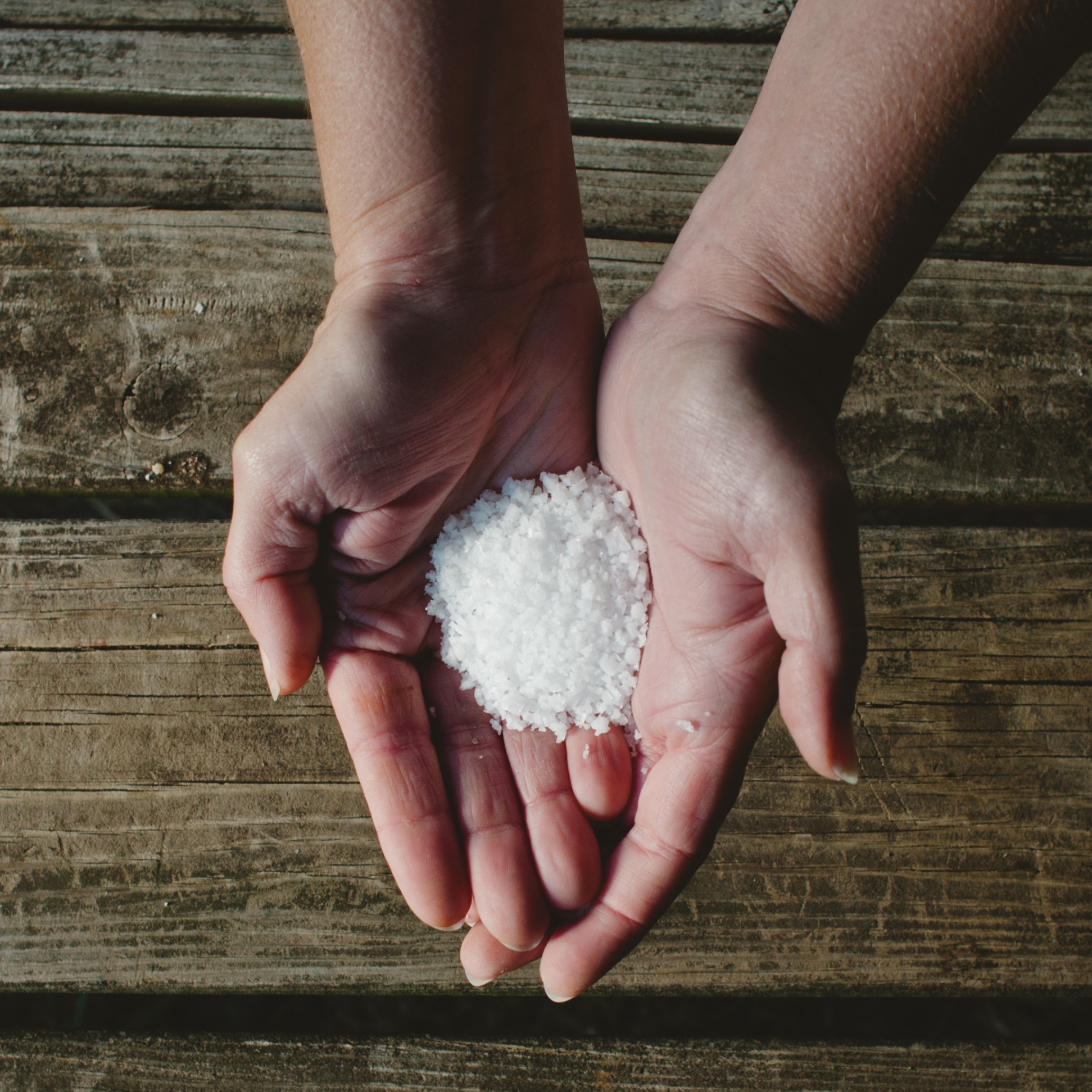 Two hands hold a small pile of white salt over a wooden surface.