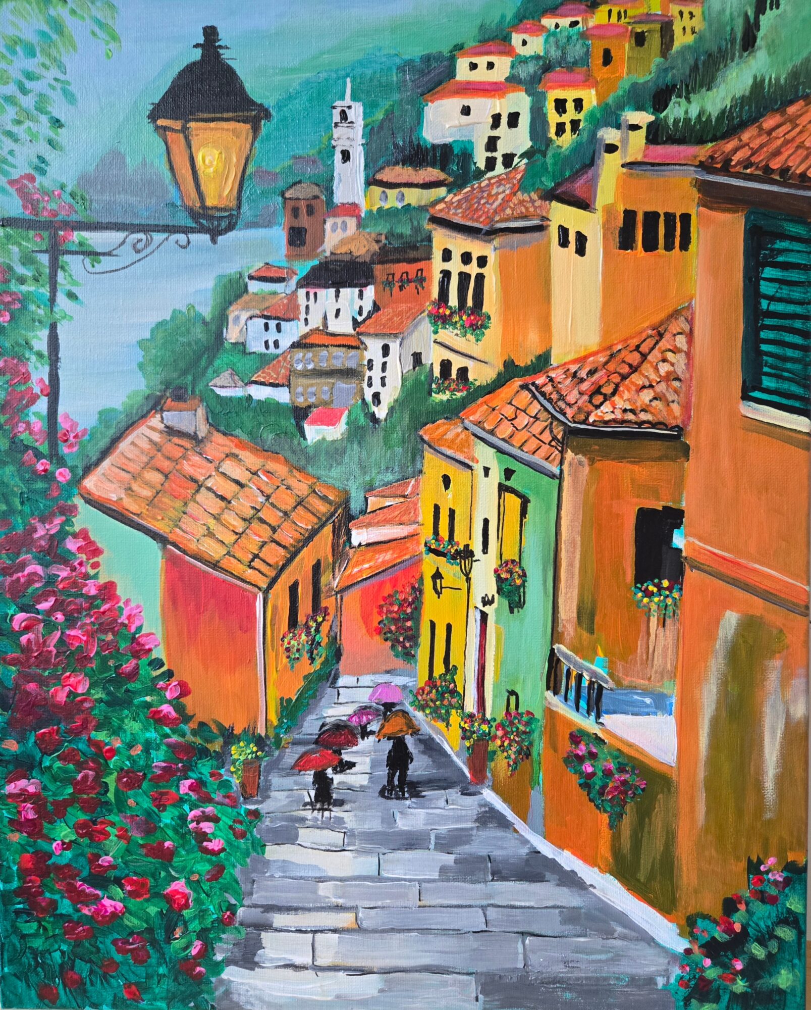 Colorful hillside village with narrow street, people walking with umbrellas, vibrant flowers, and buildings with tiled roofs.