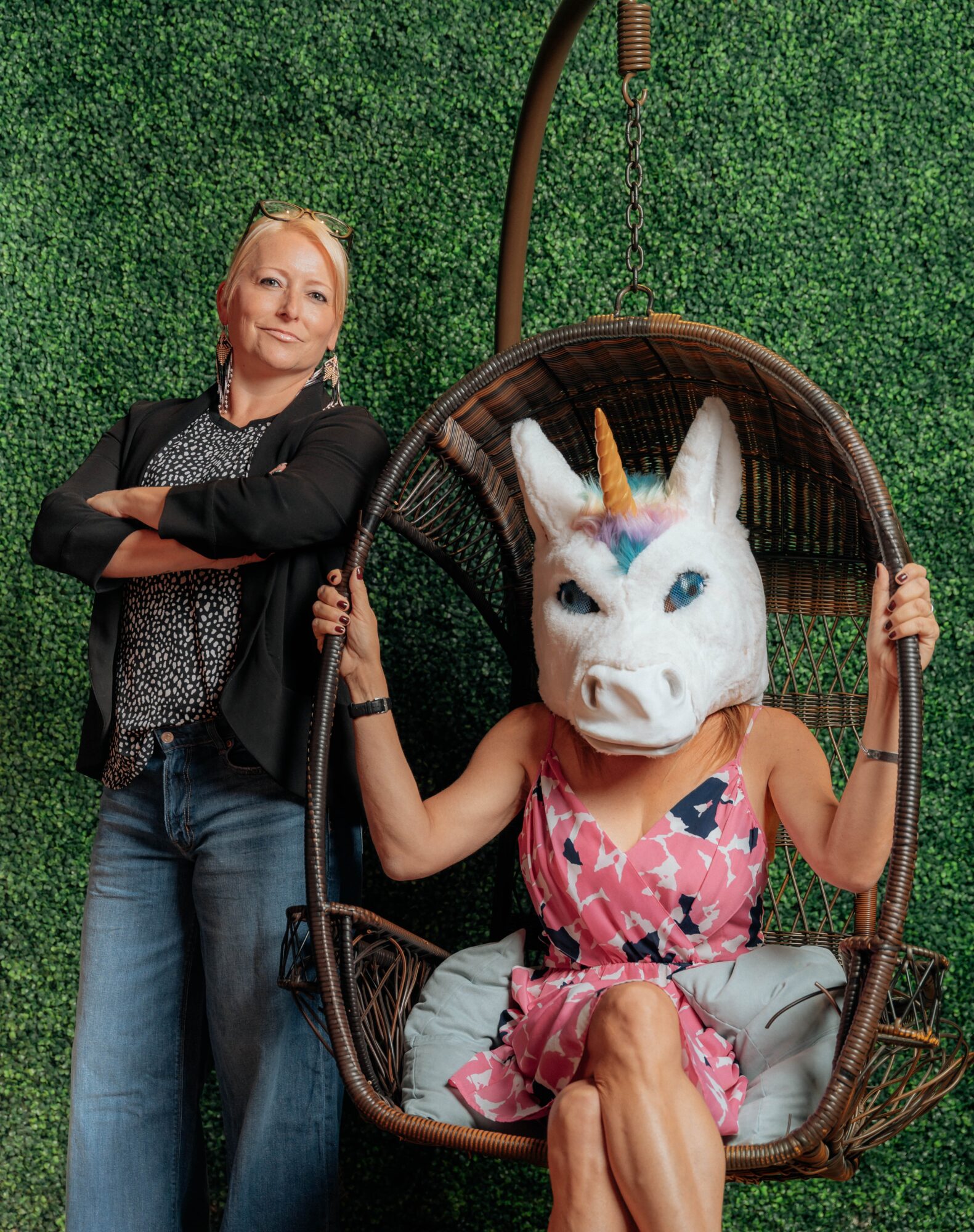 Woman standing next to a person wearing a unicorn mask sitting in a hanging chair outdoors.