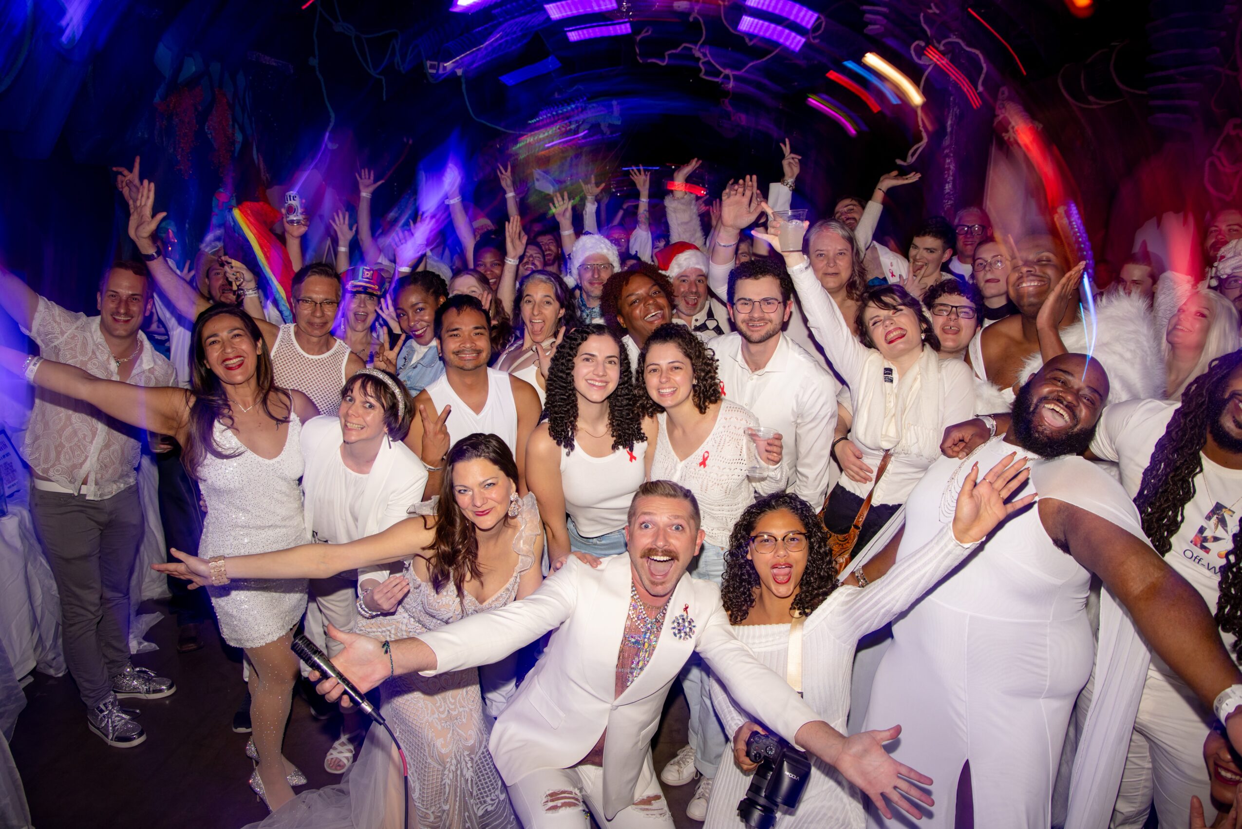 Group of people dancing and celebrating in a colorful, lively party environment with bright lights and joyful expressions.
