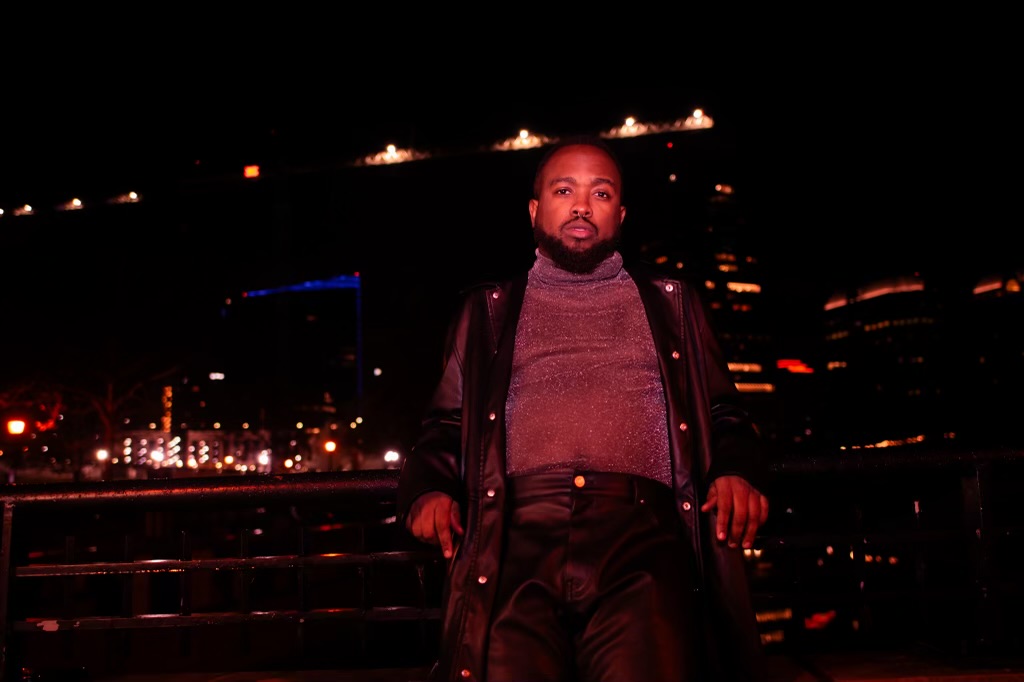 Man standing outdoors at night with city lights and buildings in the background.