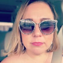 Woman with blonde hair wearing large, rhinestone sunglasses, sitting in a car, looking at the camera.
