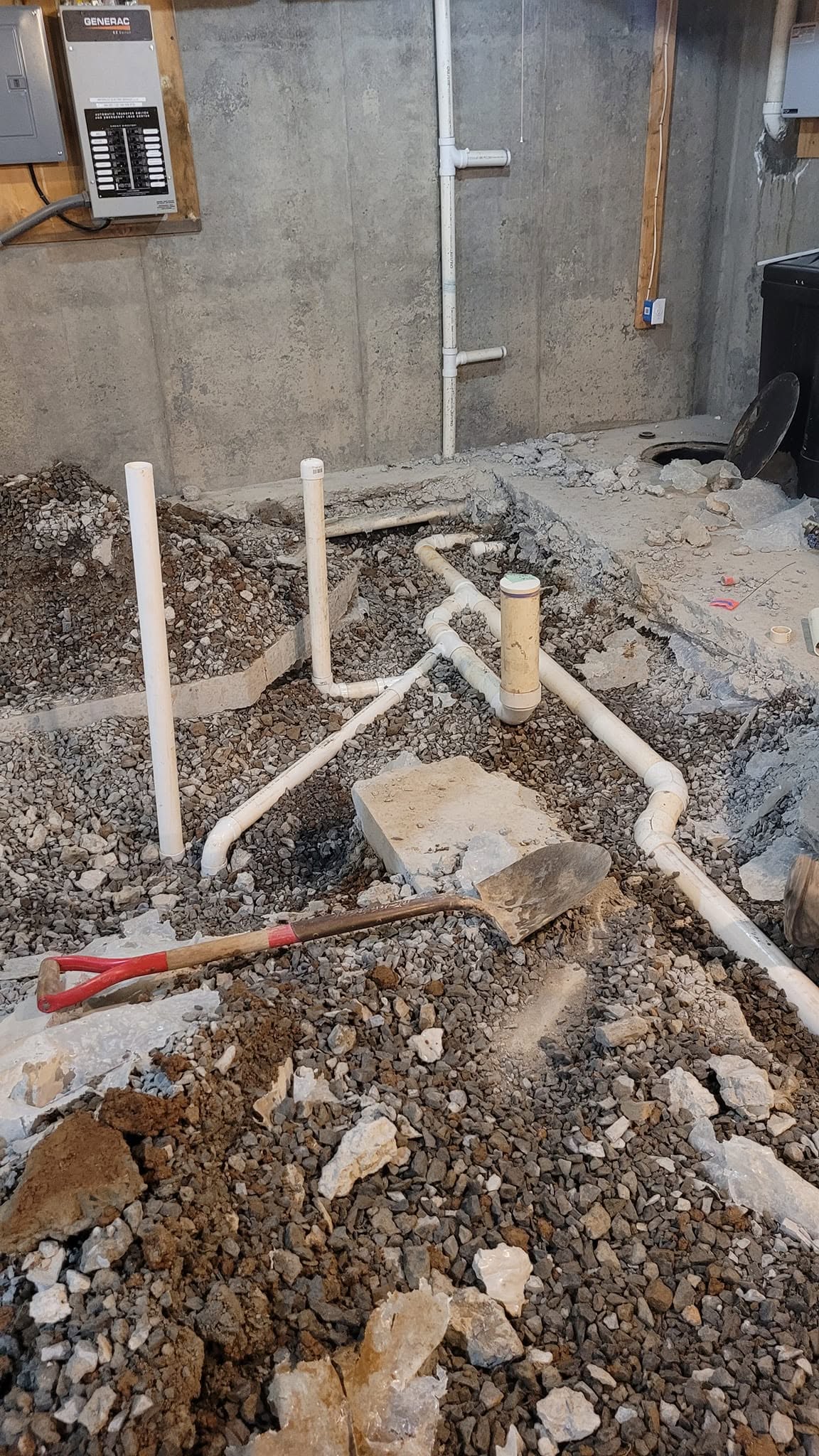 Construction site with exposed pipes and dirt, concrete wall in background, and tools on ground.