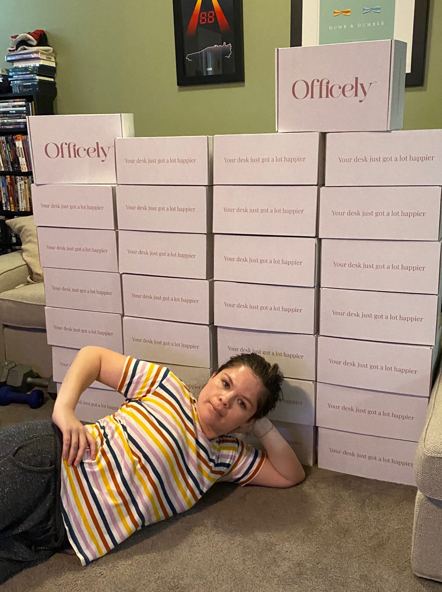 Young girl with long dark hair, wearing a striped shirt, lying on the floor next to stacked boxes, smiling.