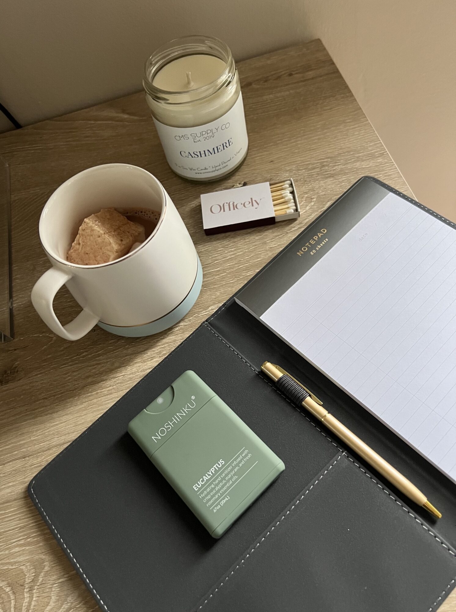 Coffee mug, notebook, pen, green soap, and a candle on a wooden surface.