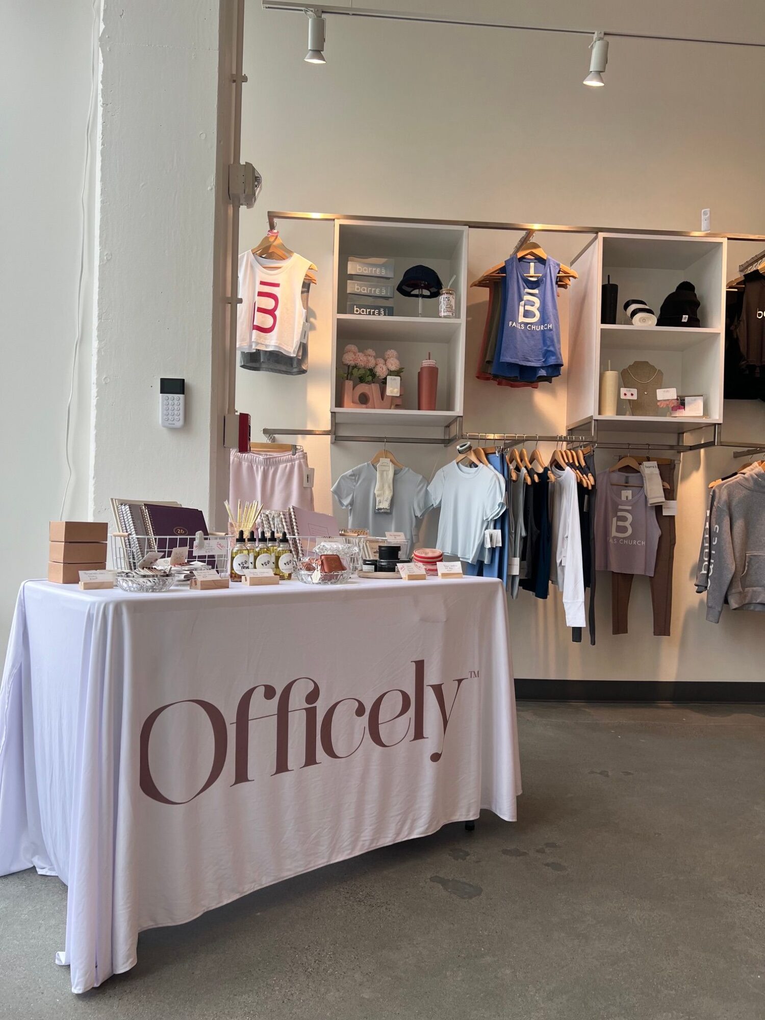 Display table with products and a large tablecloth reading 'Officelab'. Shelves with various items are behind the table.