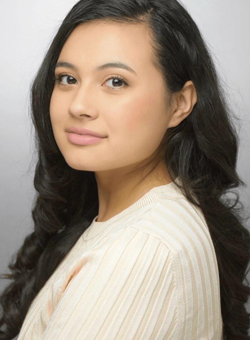 Young woman with long dark hair, wearing a light-colored top, looking at the camera with a neutral expression.