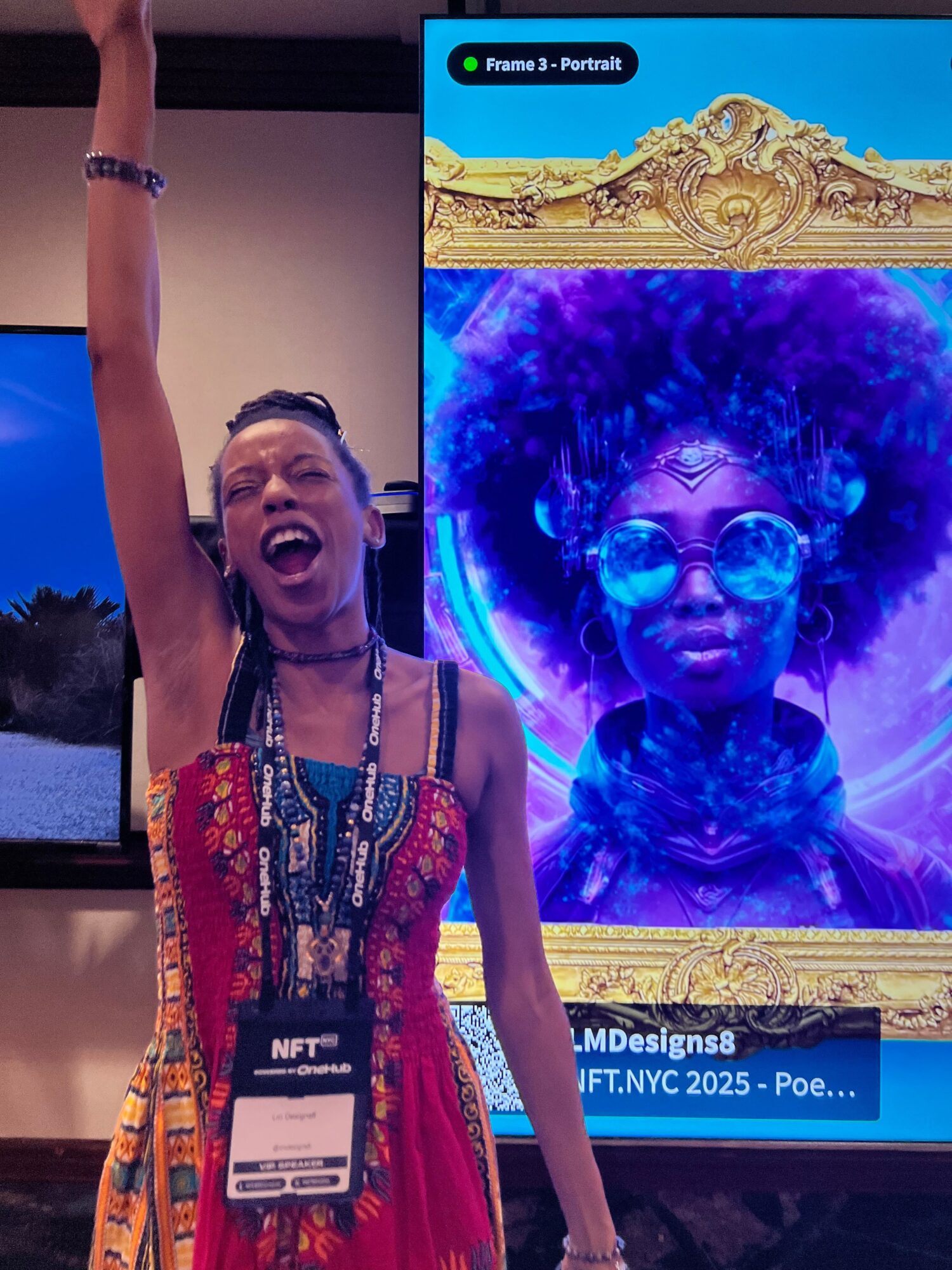 Person with arm raised, wearing colorful clothing, standing in front of a large screen displaying a vibrant, artistic image of a face with glasses.
