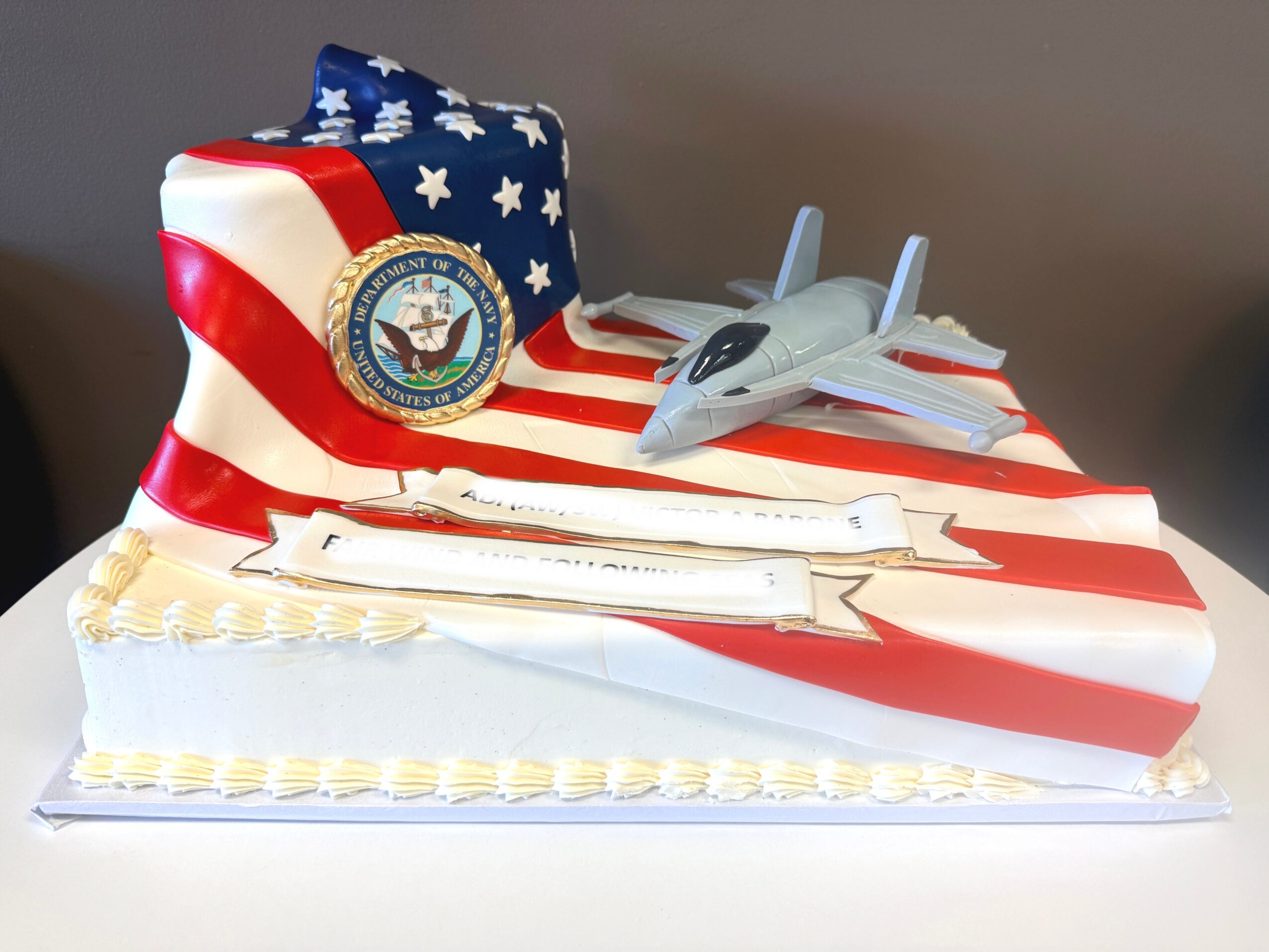 Cake decorated with American flag design, a seal, and a toy jet on top, celebrating a patriotic or military event.