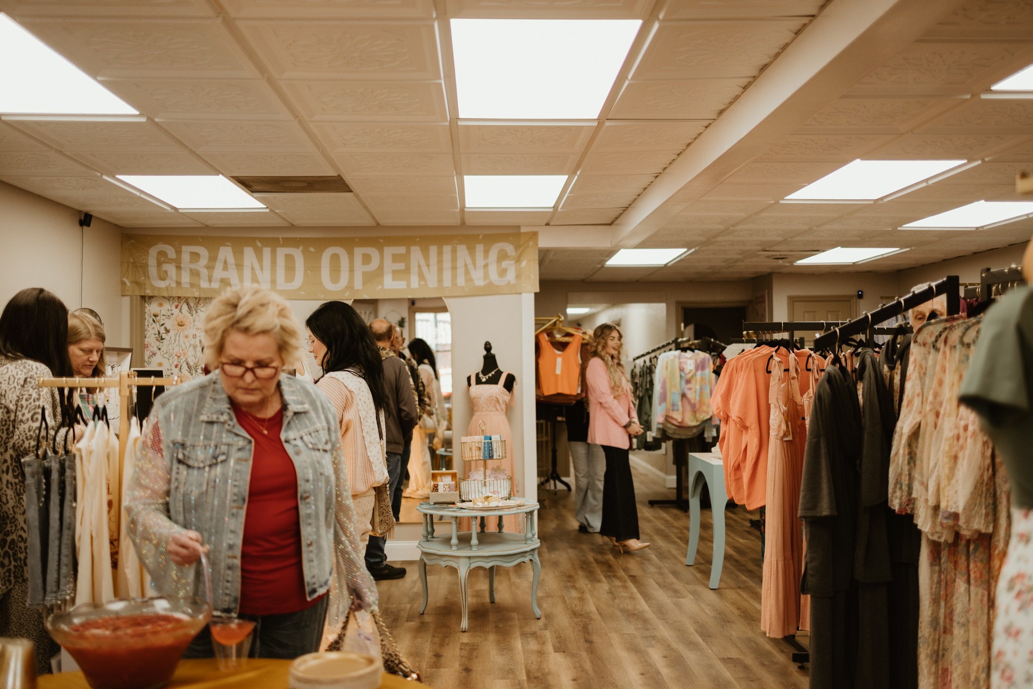 People shopping inside a clothing store with a grand opening sign, racks of clothes, and wooden flooring.