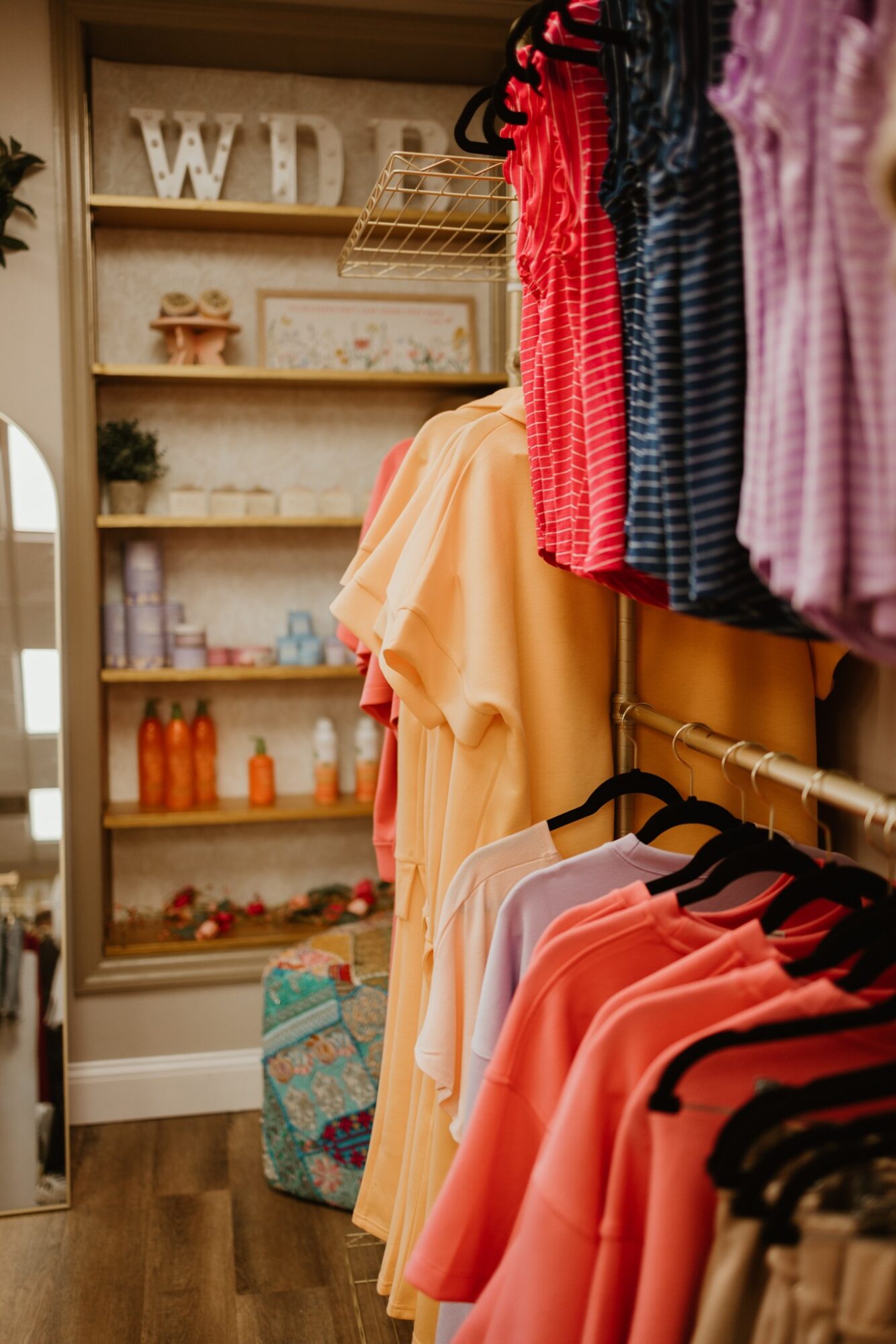 Clothing rack with colorful shirts and dresses in a store, shelves with decorative items in the background.