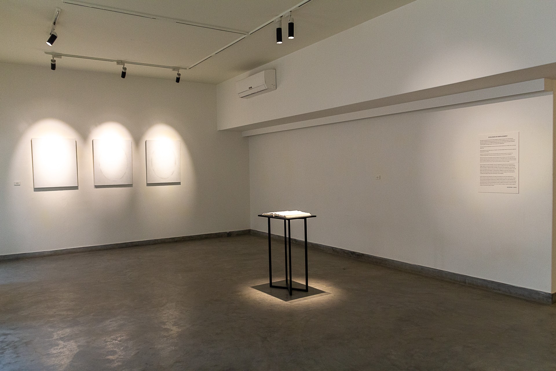 Empty art gallery with three illuminated artworks on the wall and a small table in the center, with a white wall and ceiling.