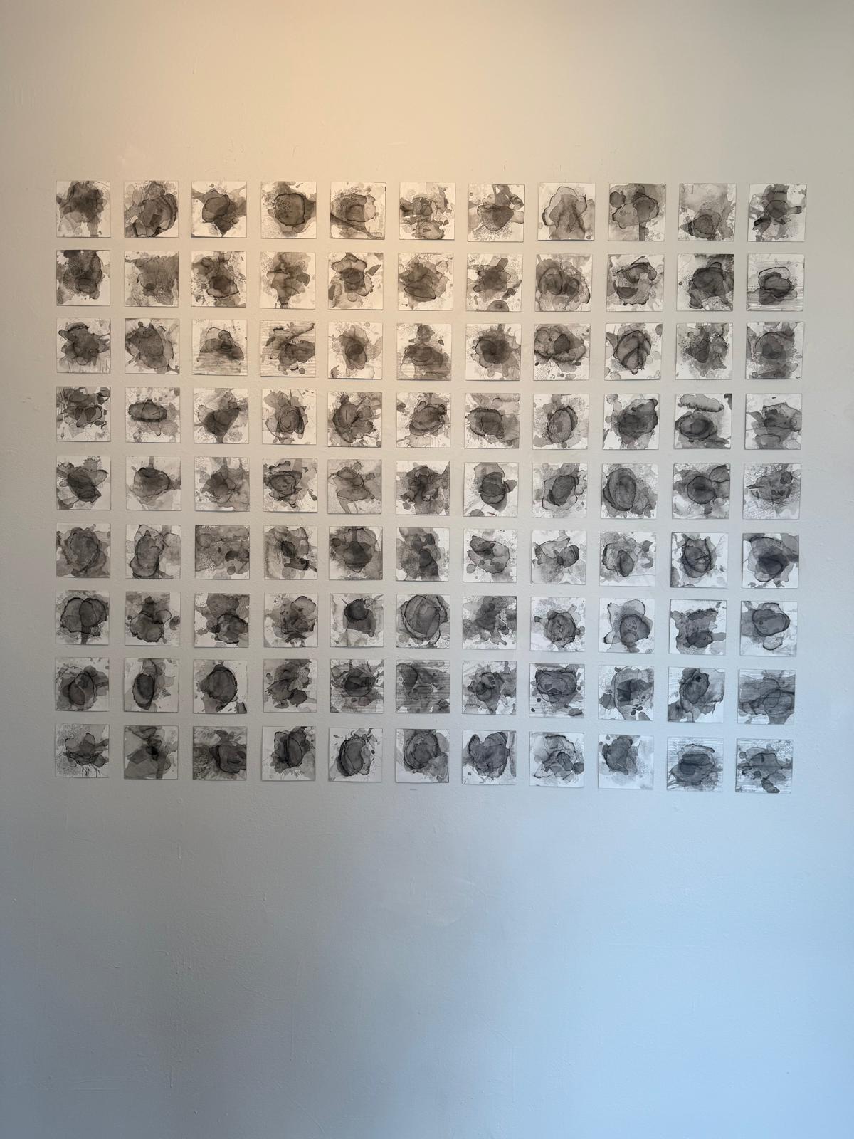 Sheet of 64 small black and white photographs arranged in an 8x8 grid on a wall.