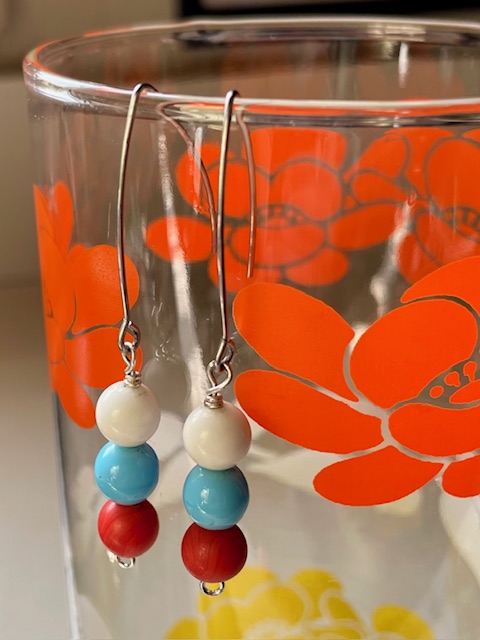 Pair of earrings with white, blue, and red beads hanging on a glass with orange floral design, close-up.