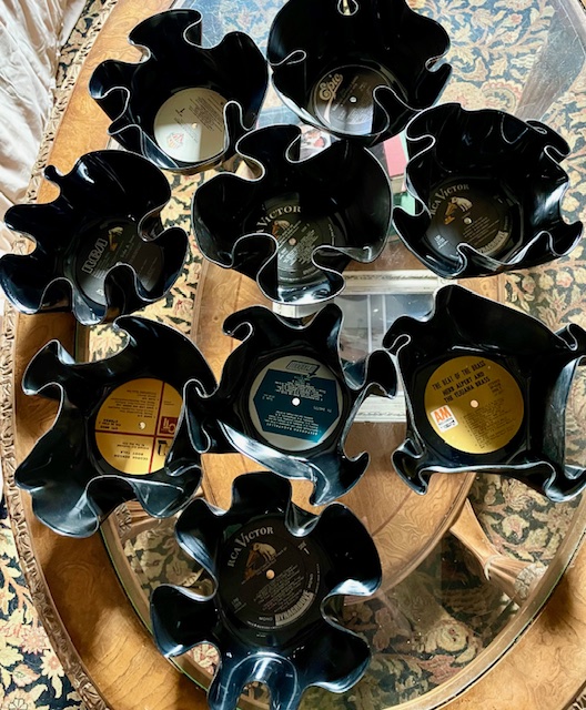 Nine black flower-shaped containers with labels, arranged on a wooden table, some with visible labels and contents.