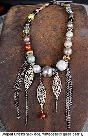 Draped chains necklace with faux pearls, vintage beads, and dangling chain elements on a wooden surface.