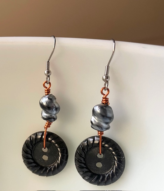 Pair of earrings with black circular pendants and silver beads, hanging from hooks, against a white background.