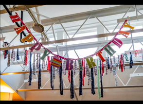 Colorful birthday banner with letters spelling 'HAPPY BIRTHDAY' hanging from ceiling, decorated with ribbons and streamers.