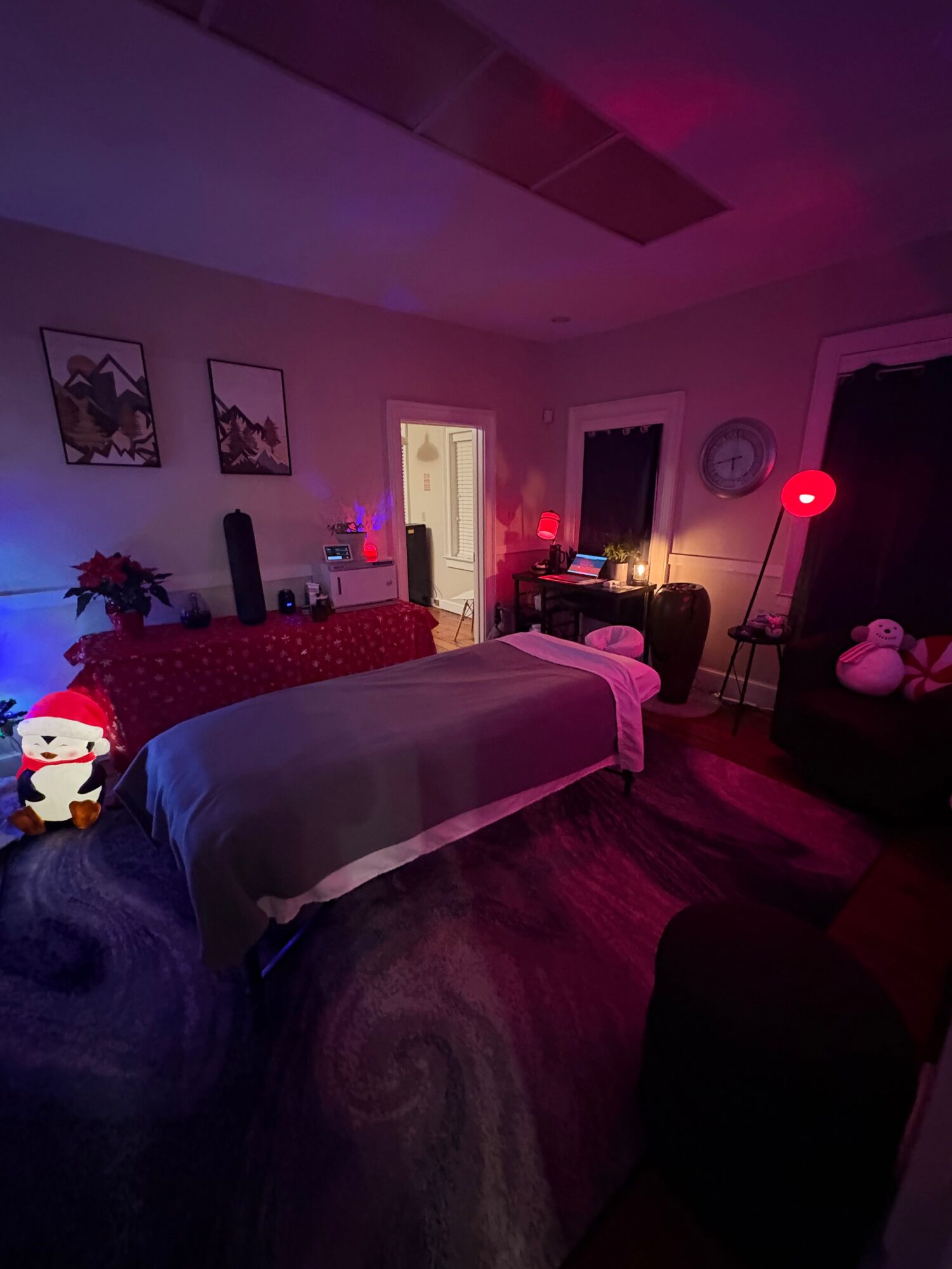 Living room with a bed, Christmas decorations, and a window, illuminated by pink and purple lighting.