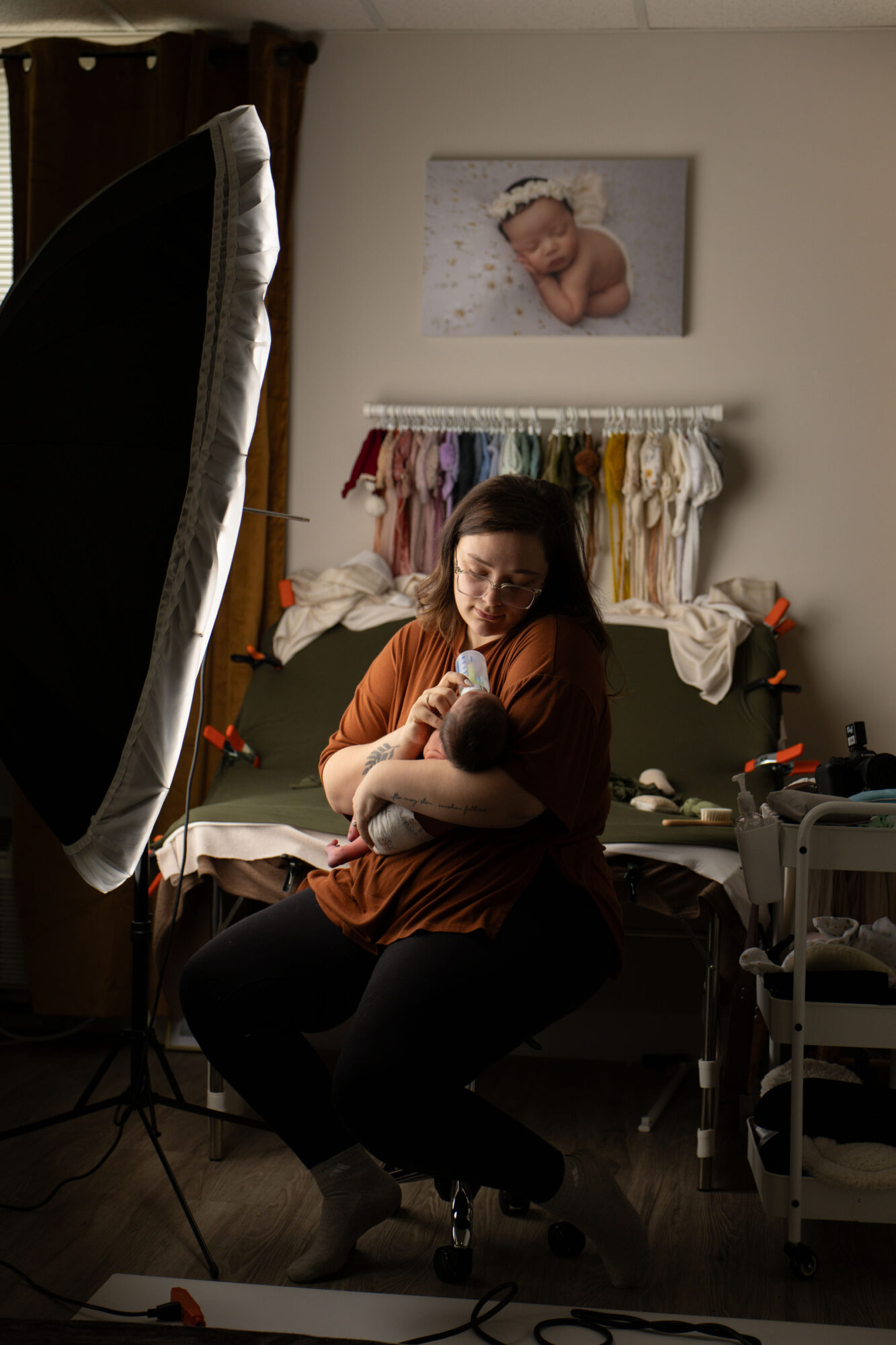 Woman sitting on a chair holding a cat in a room with a bed, clothes, and a large photo of a baby on the wall.