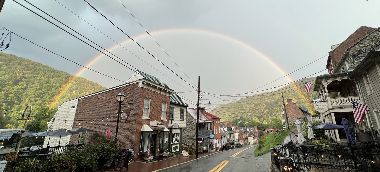 Rainbow arching over a small town street with buildings and hills in the background.