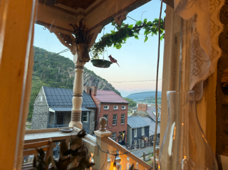 View through a window showing buildings, a mountain, and the sea in the distance, with curtains and decorative elements.