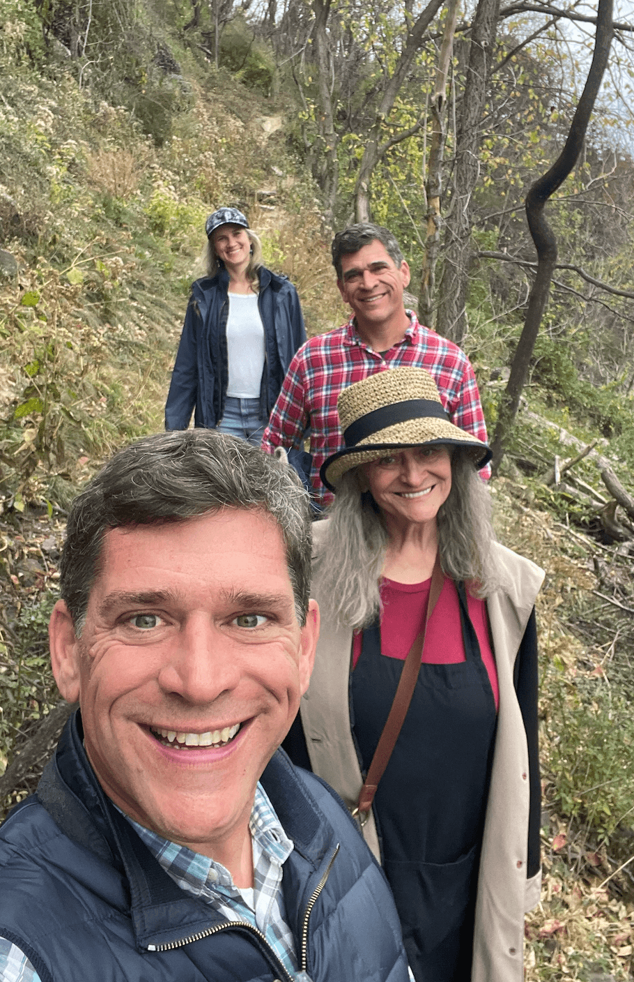 Four people outdoors in a wooded area, smiling and posing for a photo.