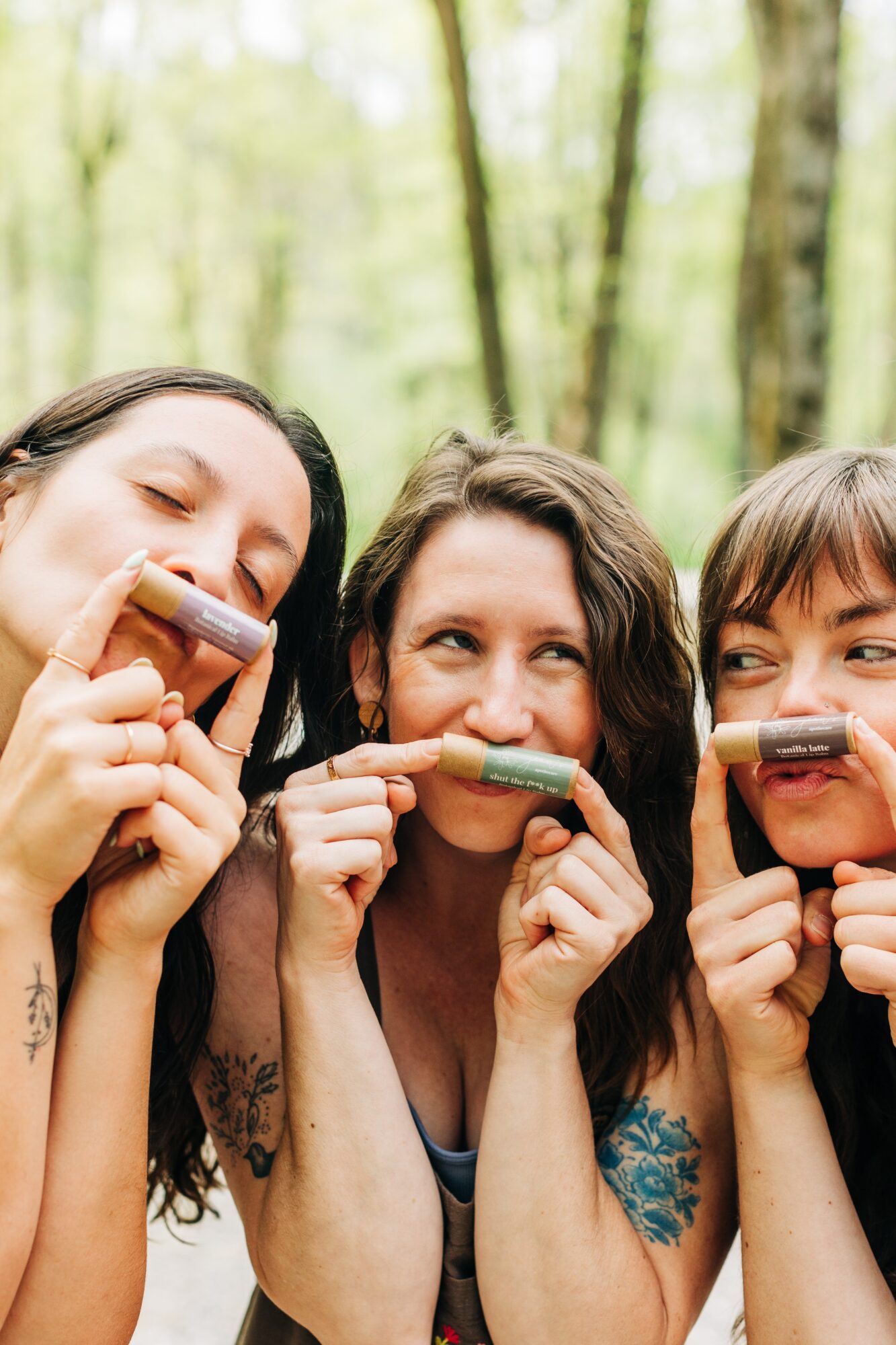 Three women smiling and holding popsicles in a forest setting.