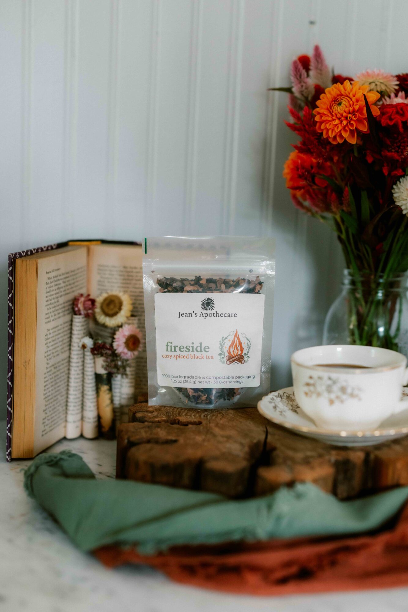 Books, a bag of fireseed, a teacup with saucer, and a bouquet of flowers on a wooden surface.