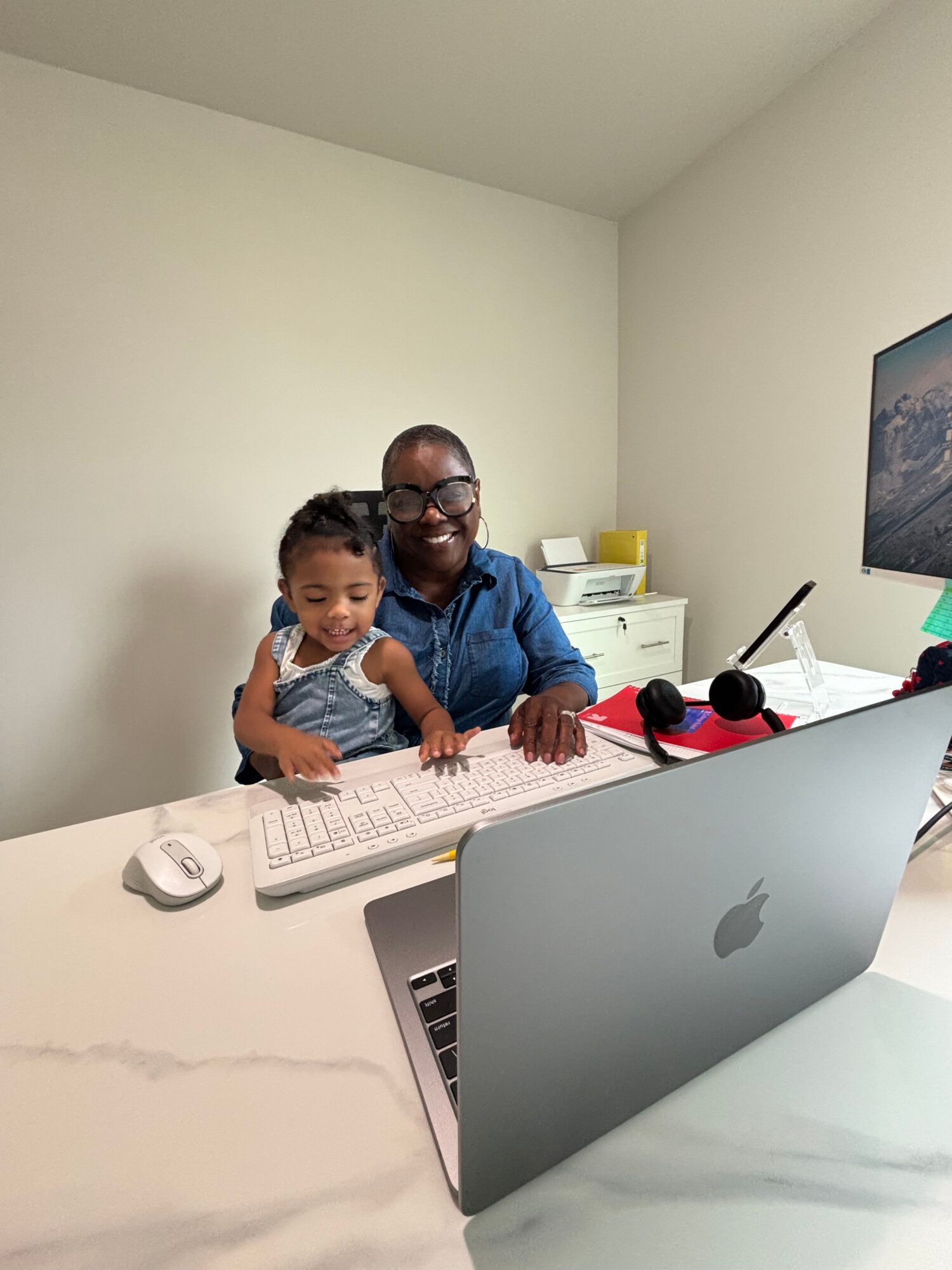 Two children sit at a desk with a laptop, microphone, and other items, looking at the camera and smiling.