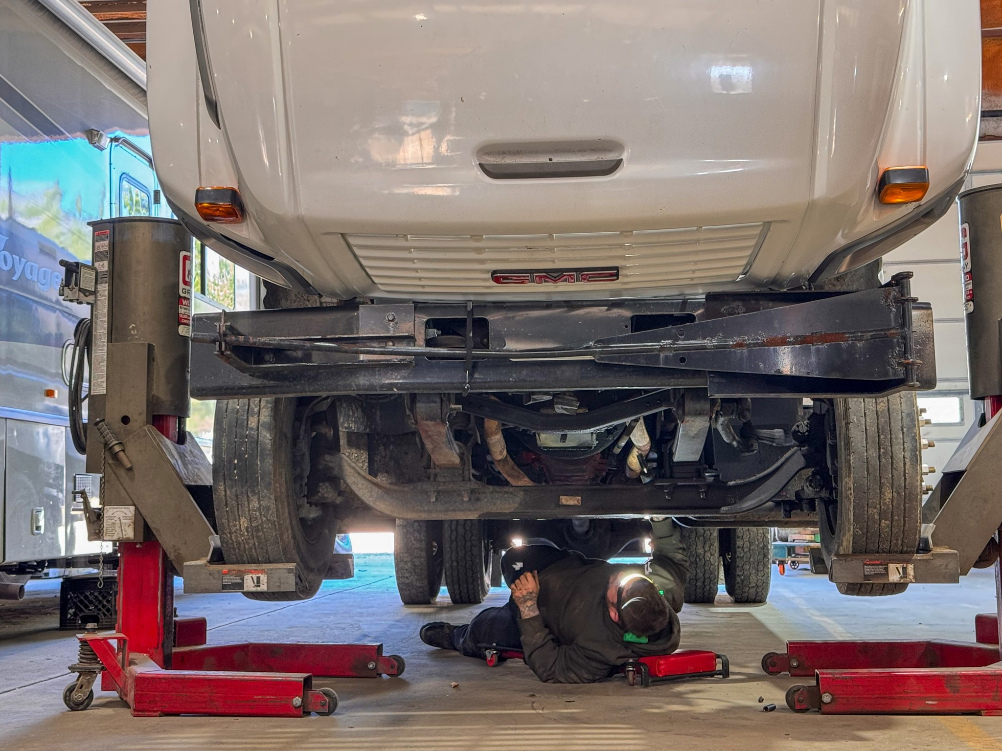 Person lying on the ground working underneath a vehicle lifted on a hydraulic lift in a garage.
