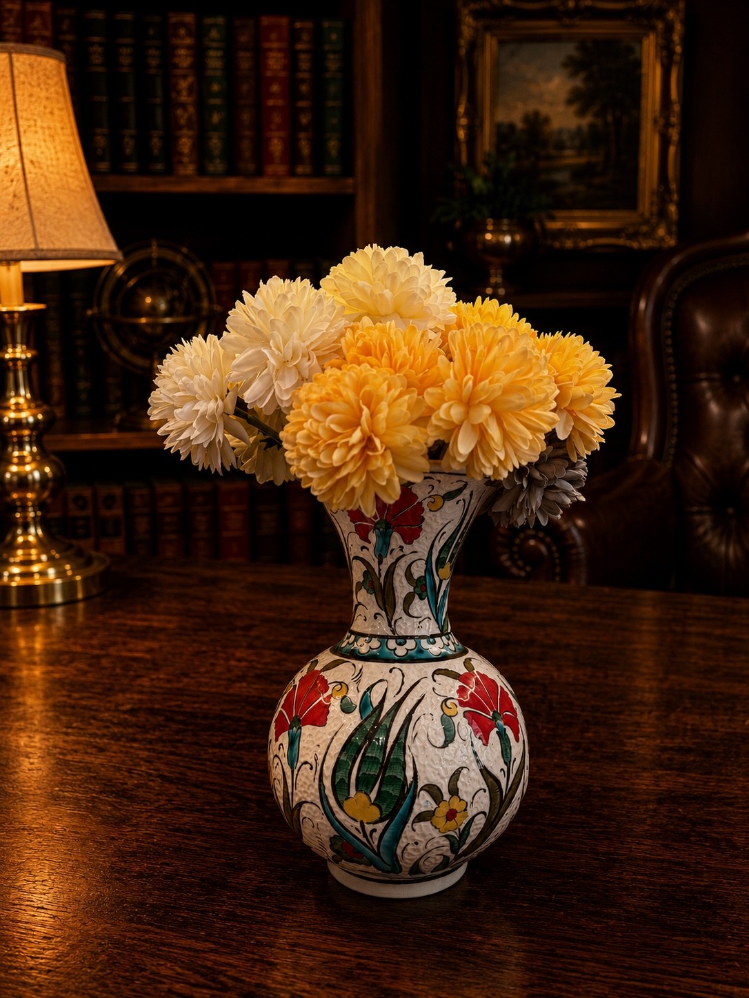 Vase with yellow and white flowers on a wooden table, dimly lit room with a lamp, bookshelf, and framed painting in background.