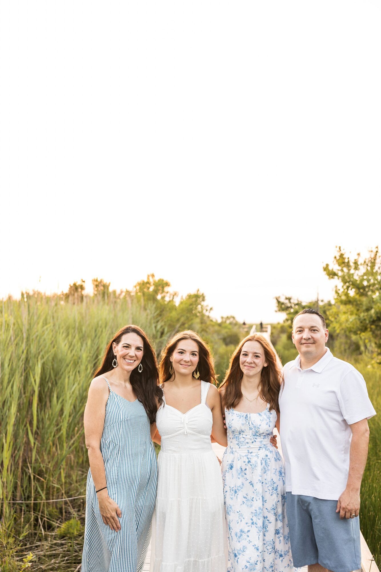 Four people standing outdoors in a grassy area with trees, smiling, with a clear sky above.