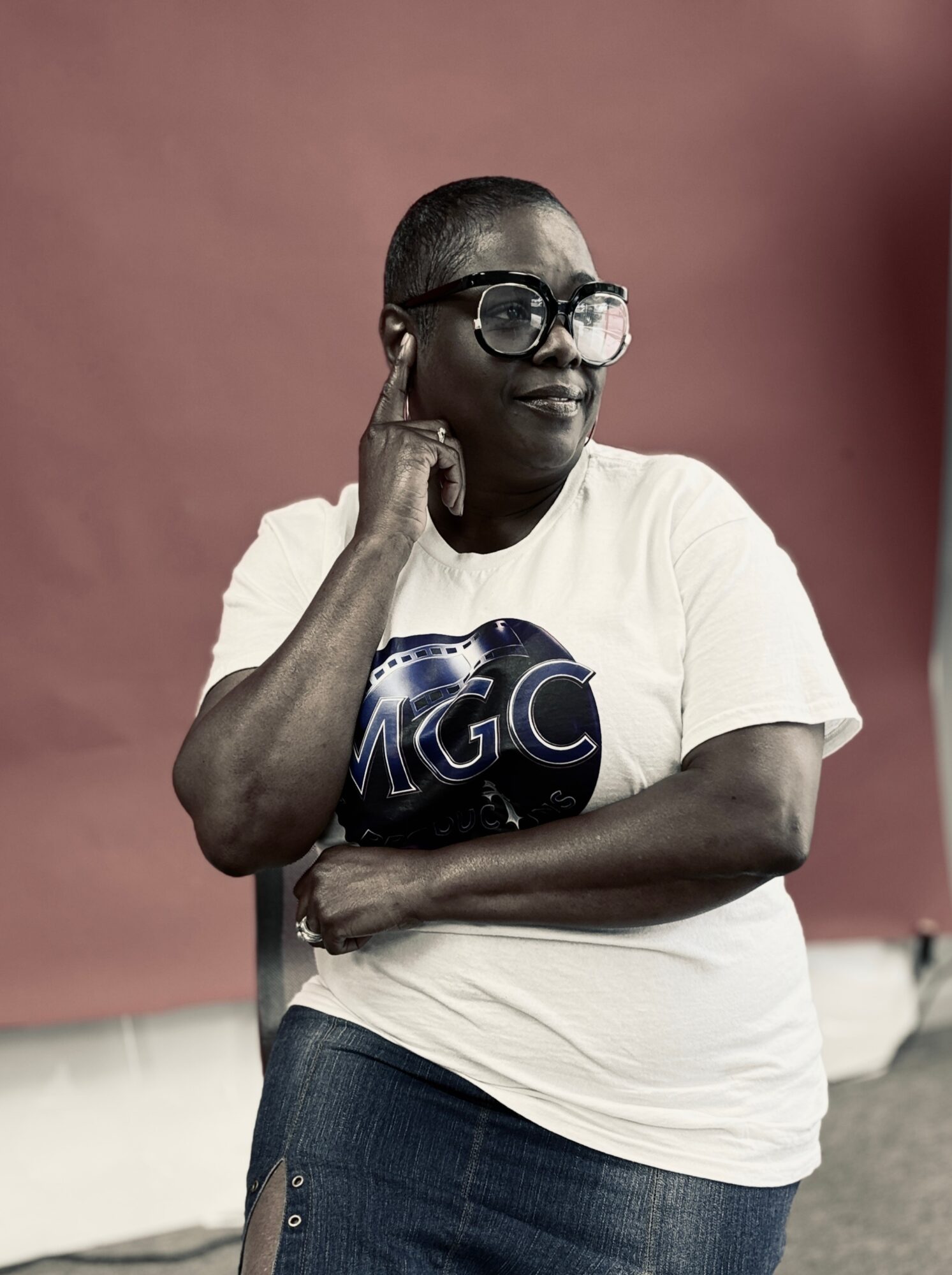 Woman with short hair and glasses, wearing a white T-shirt with a graphic, standing with arms crossed against a plain background.