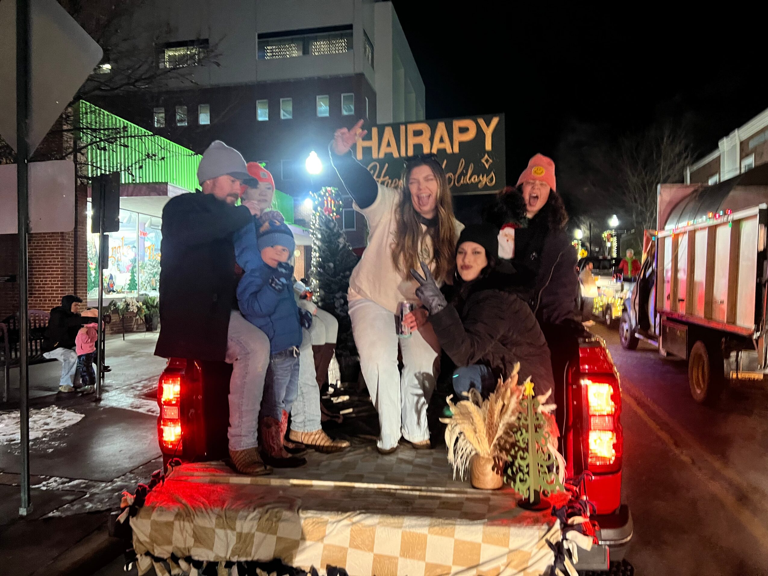 Group of people, including children, gathered on a truck bed at night, with buildings and streetlights in the background.