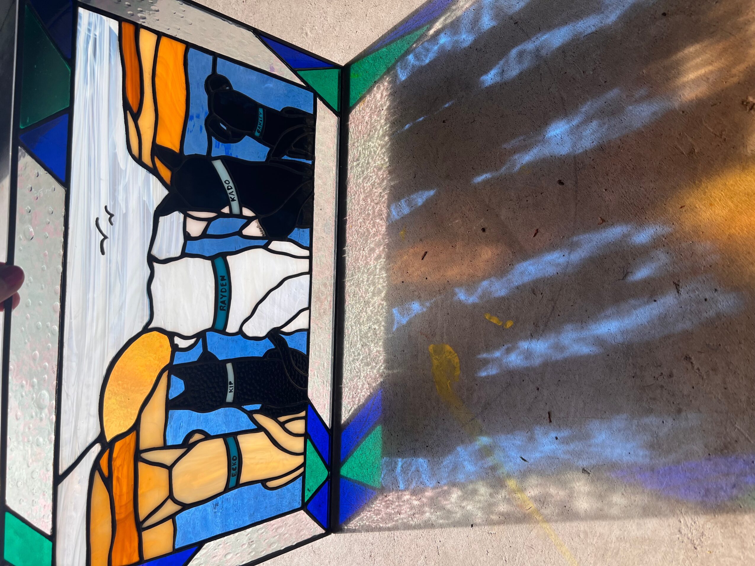 Colorful stained glass window with abstract shapes and patterns, casting reflections on a surface nearby.