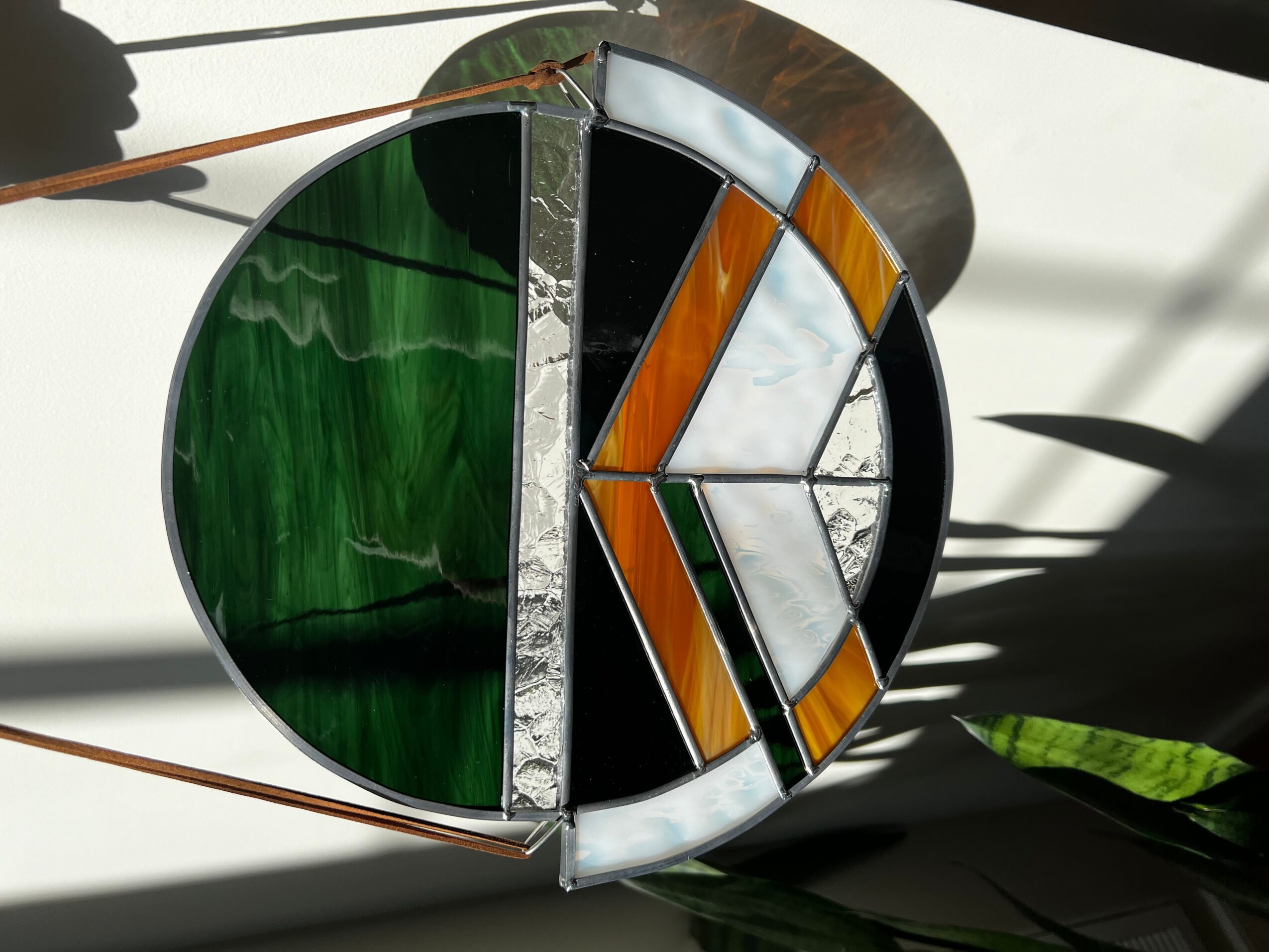 Circular stained glass window with green, black, white, and orange sections, casting shadows on a white surface.