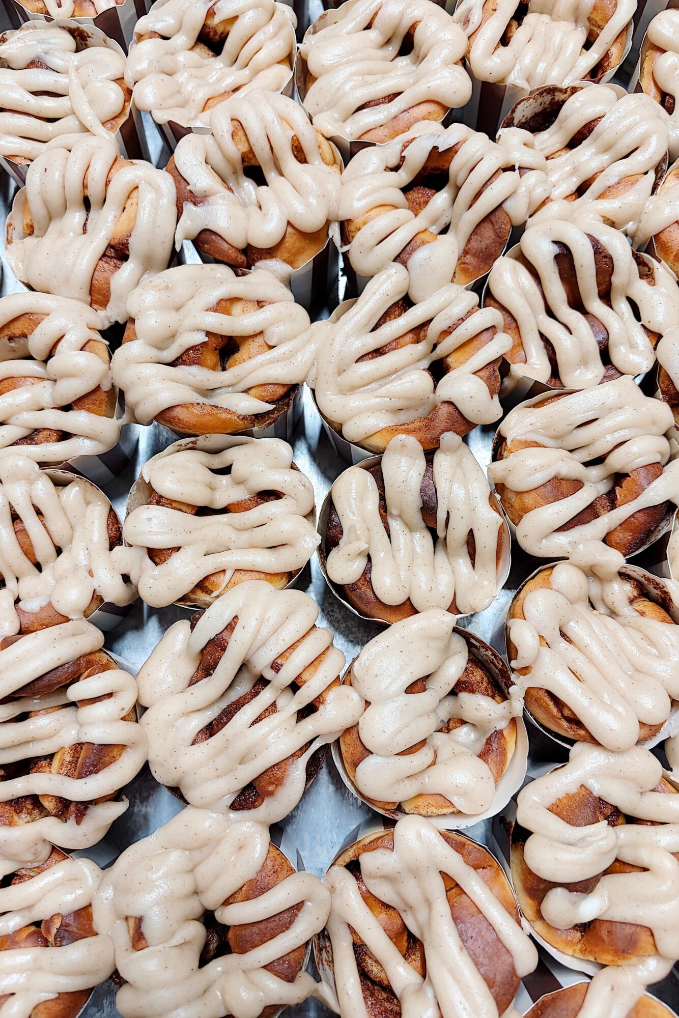 Close-up of numerous small pastries with white icing and caramel drizzle, arranged closely together.