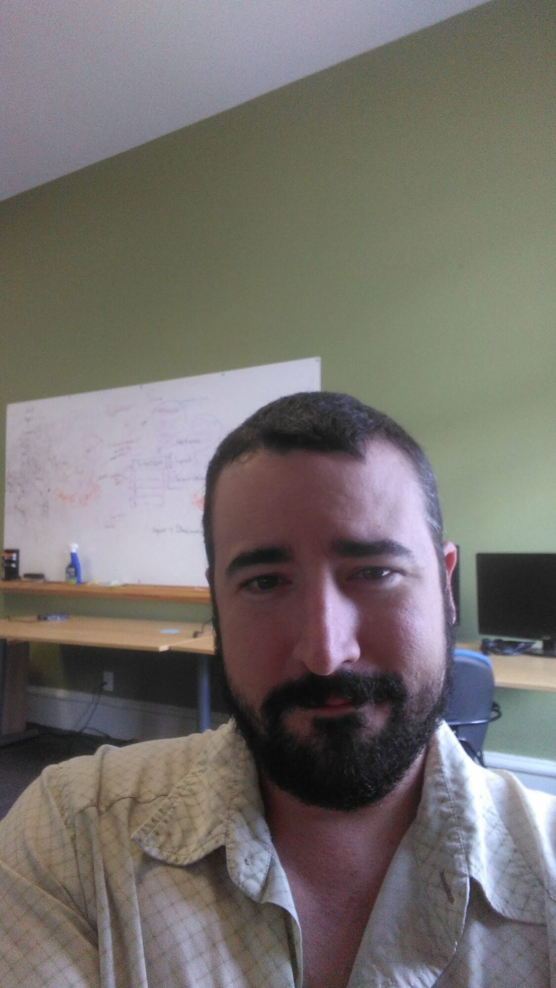 Portrait of a man with a beard and short hair, wearing a light-colored shirt, in an indoor setting.