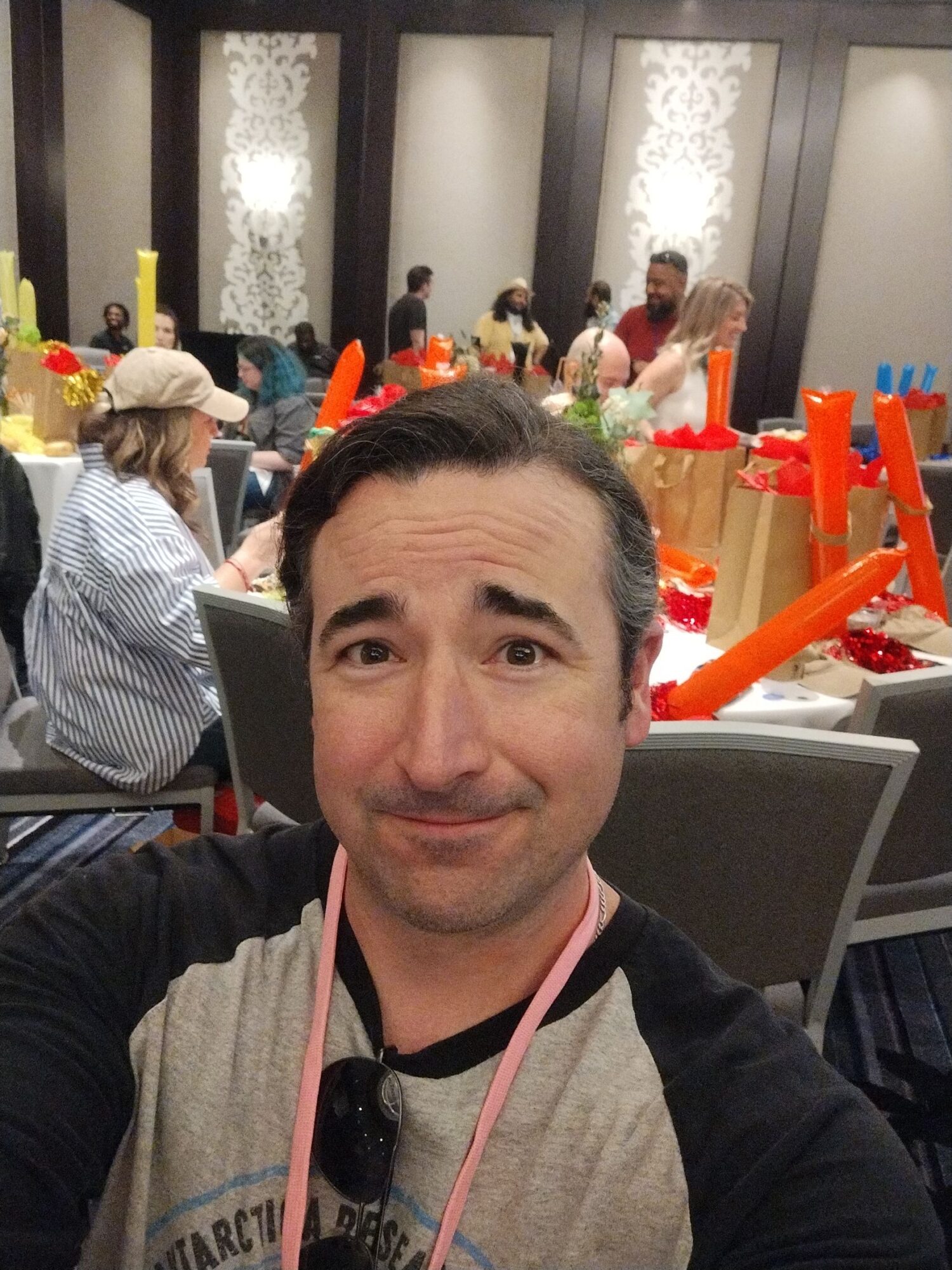 Man taking selfie in a decorated room with people and colorful decorations in the background.