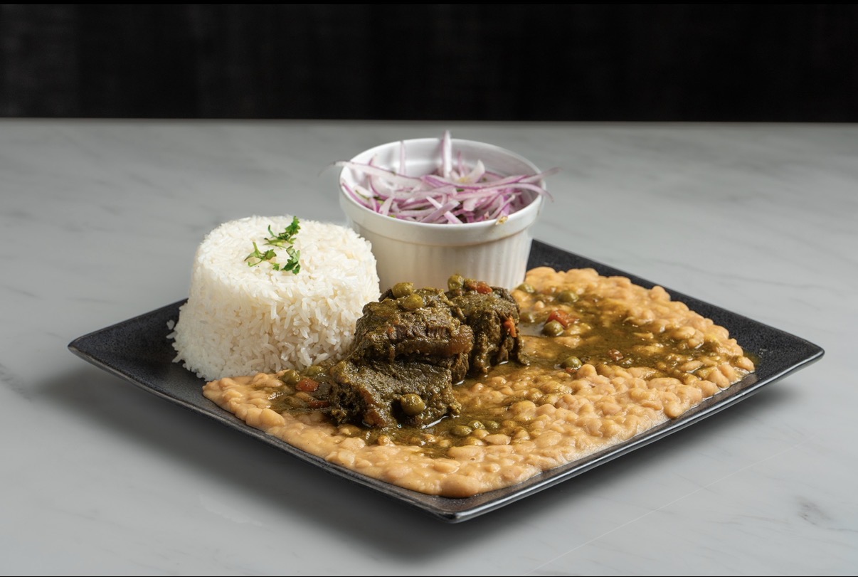 Plate with rice, beans, meat, and a cup of pinkish beverage on a marble surface.